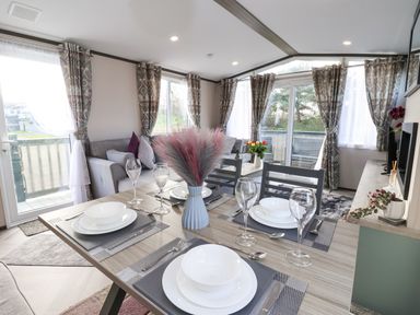 A dining table set for four with plates glasses and cutlery in a living room with sofas and curtains at Ginger Fox Lodge in East Heslerton near Cayton