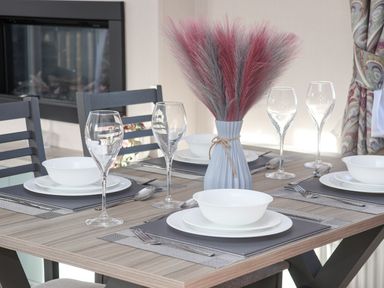 A dining table set with white plates bowls silverware and wine glasses with a vase of pink and gray dried flowers at Ginger Fox Lodge in East Heslerton near Cayton