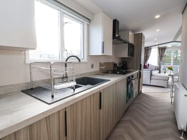 A kitchen with a sink drying rack and oven leading to a living room at Ginger Fox Lodge in East Heslerton near Cayton