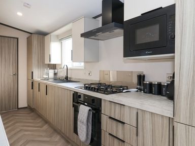 A kitchen with wooden cabinets a gas stove an oven a microwave and containers labeled tea sugar and coffee at Ginger Fox Lodge in East Heslerton near Cayton