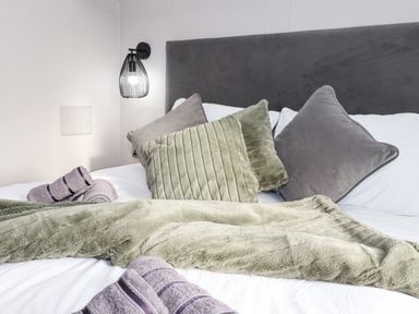 A bed with grey and green pillows and a green throw blanket with rolled purple towels at Ginger Fox Lodge in East Heslerton near Cayton