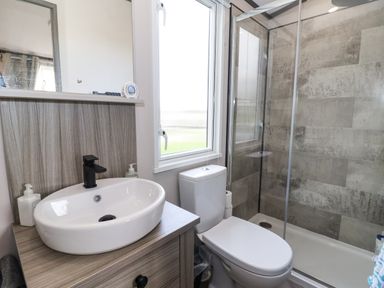 A bathroom with a sink, toilet, window, and shower with tiled walls at Ginger Fox Lodge in East Heslerton near Cayton