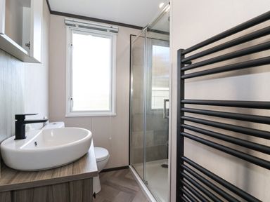 A bathroom with a sink, toilet, shower enclosure, and a black heated towel rail at Ginger Fox Lodge in East Heslerton near Cayton