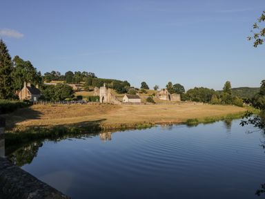 A river in front of fields with ruins and houses in the background at Ginger Fox Lodge in East Heslerton near Cayton