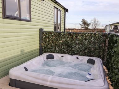An outdoor hot tub with bubbling water next to a light green cabin with a privacy screen covered in artificial leaves at Ginger Fox Lodge in East Heslerton near Cayton