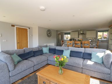 A living room with a grey sectional sofa and a wooden coffee table with flowers at Curtau Llanfaredd near Builth Wells