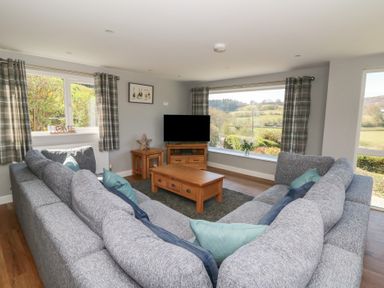 A living room with grey sofas a wooden coffee table and TV with large windows showing countryside views at Curtau in Llanfaredd near Builth Wells
