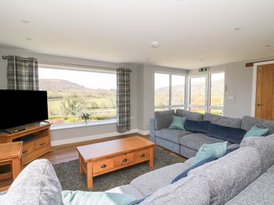 A living room with gray sofas and wooden tables facing large windows showing a landscape at Curtau in Llanfaredd near Builth Wells