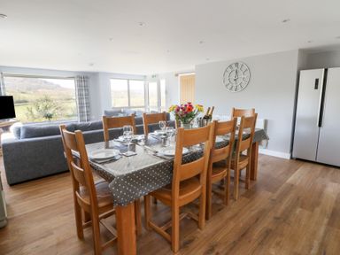 A dining area with a wooden table set with plates and glasses next to a sitting area with gray sofas at Curtau in Llanfaredd near Builth Wells