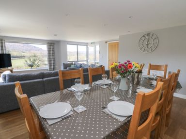A dining table with plates glasses and flowers in a living room with sofas and large windows at Curtau Llanfaredd near Builth Wells