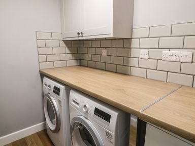 A laundry room with a washing machine and dryer under a wooden countertop with white cabinets above at Curtau in Llanfaredd near Builth Wells