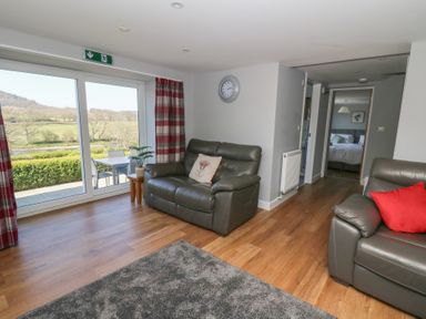 A living room with leather sofas and a sliding glass door leading to a patio at Curtau Llanfaredd near Builth Wells