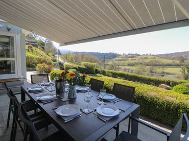 An outdoor dining table set with plates glasses and cutlery under an awning overlooking a garden and countryside at Curtau Llanfaredd near Builth Wells
