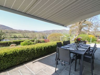 An outdoor dining area with a table set with plates and glasses under a retractable awning overlooking a garden and hills at Curtau in Llanfaredd near Builth Wells