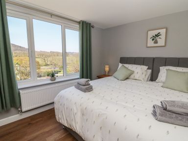 A bedroom with a double bed green curtains and a window overlooking trees at Curtau Llanfaredd near Builth Wells