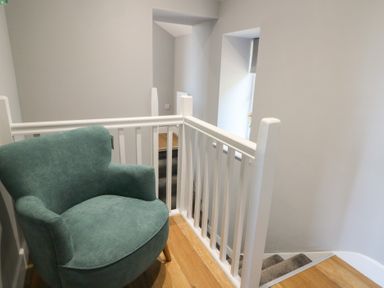 A green armchair next to a white railing on a wooden floor at Curtau in Llanfaredd near Builth Wells