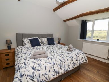 A bedroom with a double bed two bedside tables with lamps wooden beams on the ceiling and a window showing a countryside view at Curtau in Llanfaredd near Builth Wells