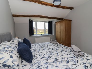 A bedroom with a bed with patterned bedding, two folded towels, wooden wardrobe, window with black curtains and exposed wooden ceiling beams at Curtau in Llanfaredd near Builth Wells