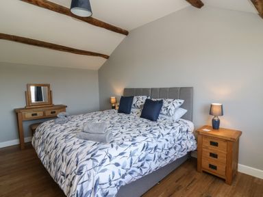 A bedroom with a large bed with patterned bedding two bedside tables with lamps and a dressing table with a mirror at Curtau Llanfaredd near Builth Wells