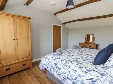 A bedroom with a wooden wardrobe a bed with patterned bedding and a wooden dressing table with a mirror at Curtau Llanfaredd near Builth Wells