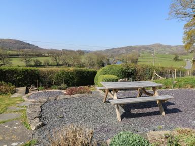 An outdoor area with a wooden picnic table on a gravel surface overlooking hedges and hills at Curtau Llanfaredd near Builth Wells