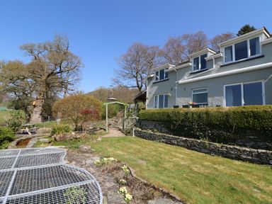 A garden with a lawn and stone path beside a house with large windows at Curtau in Llanfaredd near Builth Wells