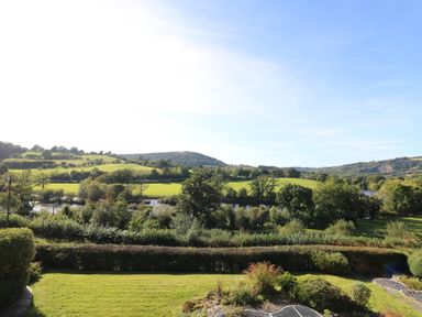 A garden with bushes and a lawn overlooking a river and green hills at Curtau in Llanfaredd near Builth Wells