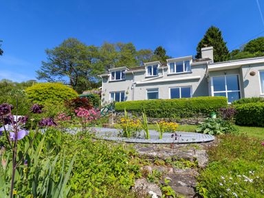 A garden with flowers and bushes in front of a two-story house with multiple windows at Curtau in Llanfaredd near Builth Wells