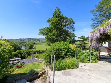A garden with plants trees and flowering vines next to a stone patio and a river in the background at Curtau Llanfaredd near Builth Wells