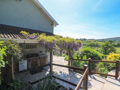 An outdoor bbq area with flowers hanging above next to a garden and a view of green fields at Curtau Llanfaredd near Builth Wells