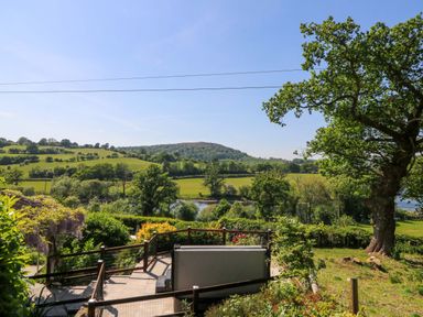 A garden with a hot tub overlooking green fields trees and a river at Curtau Llanfaredd near Builth Wells