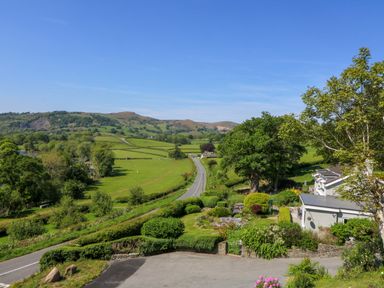 A rural road with green fields trees and houses under a clear blue sky at Curtau Llanfaredd near Builth Wells