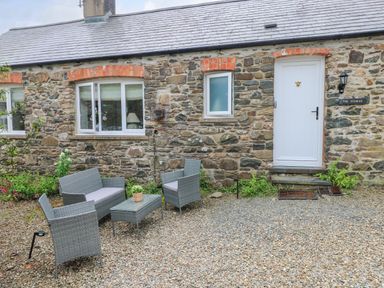An outdoor seating area with a sofa table and chairs in front of a stone building with white windows and door at The Stables Near Solva