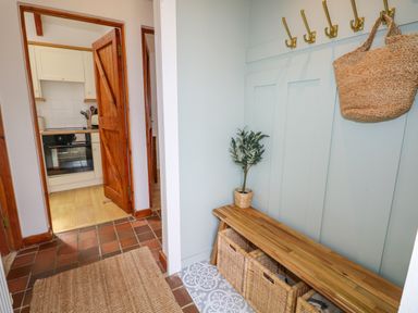 A hallway with wooden bench and baskets with hooks on the wall and a view into a kitchen at The Stables Near Solva