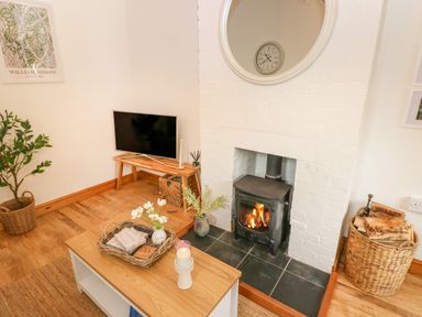 A corner living room with a wood stove fireplace a television on a wooden stand a coffee table with a candle and flowers and baskets with logs near the fireplace at The Stables Near Solva