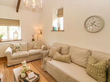 A living room with two beige sofas wooden coffee table a wall clock and windows with blinds at The Stables Near Solva
