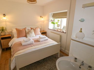 A bedroom with a double bed with towels on it bedside tables with lamps a window with flowers and a sink at The Stables Near Solva