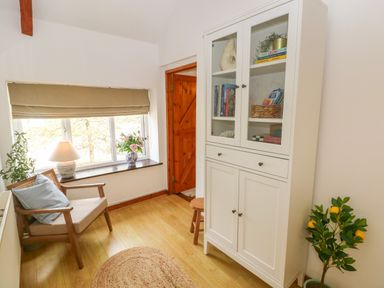 A small room with a wooden chair, white cabinet with glass doors, a window with blinds, and a plant at The Stables Near Solva