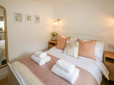A bedroom with a bed made with white and pink bedding two bedside tables and wall art at The Stables Near Solva
