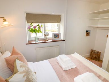 A bedroom with a bed featuring pillows and folded towels near a window with flowers and a picture frame at The Stables Near Solva