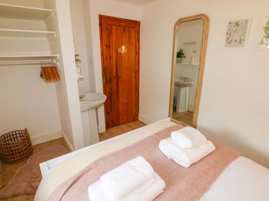 A bedroom with a bed folded towels a wooden door a sink a full length mirror and an open closet at The Stables Near Solva