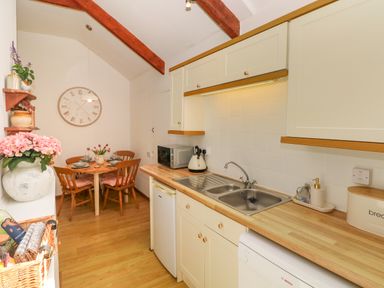 A kitchen with wooden countertops and cabinets a dining table with four chairs and a large wall clock at The Stables Near Solva
