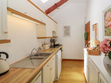 A kitchen with sink, kettle, toaster, cabinets, wooden countertop, and a basket with bottles on a sideboard at The Stables Near Solva