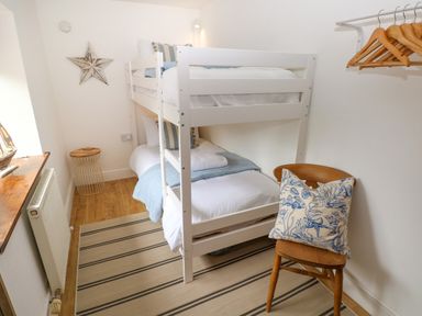 A small bedroom with a white bunk bed a wooden chair with a cushion a rug and a wall star at The Stables Near Solva