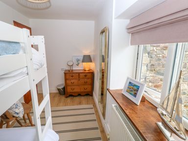 A bedroom with a bunk bed wooden dresser lamp and mirror near a window with a model boat at The Stables Near Solva