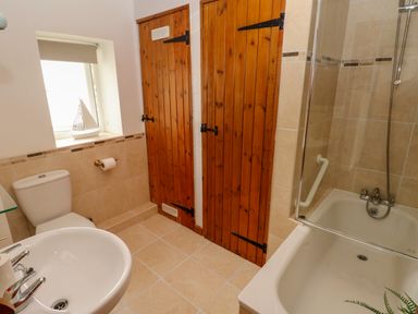 A bathroom with a sink toilet bathtub shower wooden doors and a small window near The Stables Near Solva