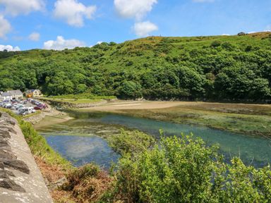 A coastal inlet with clear water surrounded by green hills and a parking area with vehicles at The Stables Near Solva