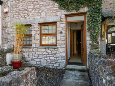 The exterior of a stone house with two windows and an open wooden door with ivy on the wall at Time and Tide in Arnside