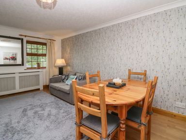 A dining area with a wooden table and chairs next to a gray sofa and a window with curtains at Time and Tide in Arnside