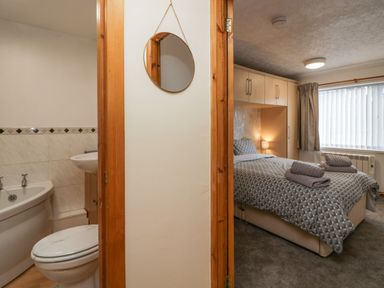 A bathroom with a bathtub and toilet on the left and a bedroom with a bed and folded towels on the right at Time and Tide in Arnside